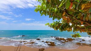 Ein Strand mit klarem, blauem Wasser, felsigem Ufer und grüner Vegetation.