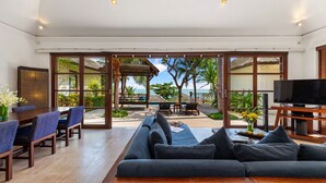 Ein geräumiger Wohnbereich mit Sofa, Esstisch, Stühlen, einem Fernseher und Meerblick durch große Glasfenster.