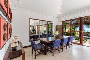 Un espace repas comprenant une longue table en bois, des chaises à l’assise rembourrée de couleur bleue et un buffet décoratif en bois.