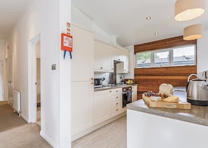 Una cocina moderna con armarios blancos, horno empotrado, microondas y una pared decorativa de madera.