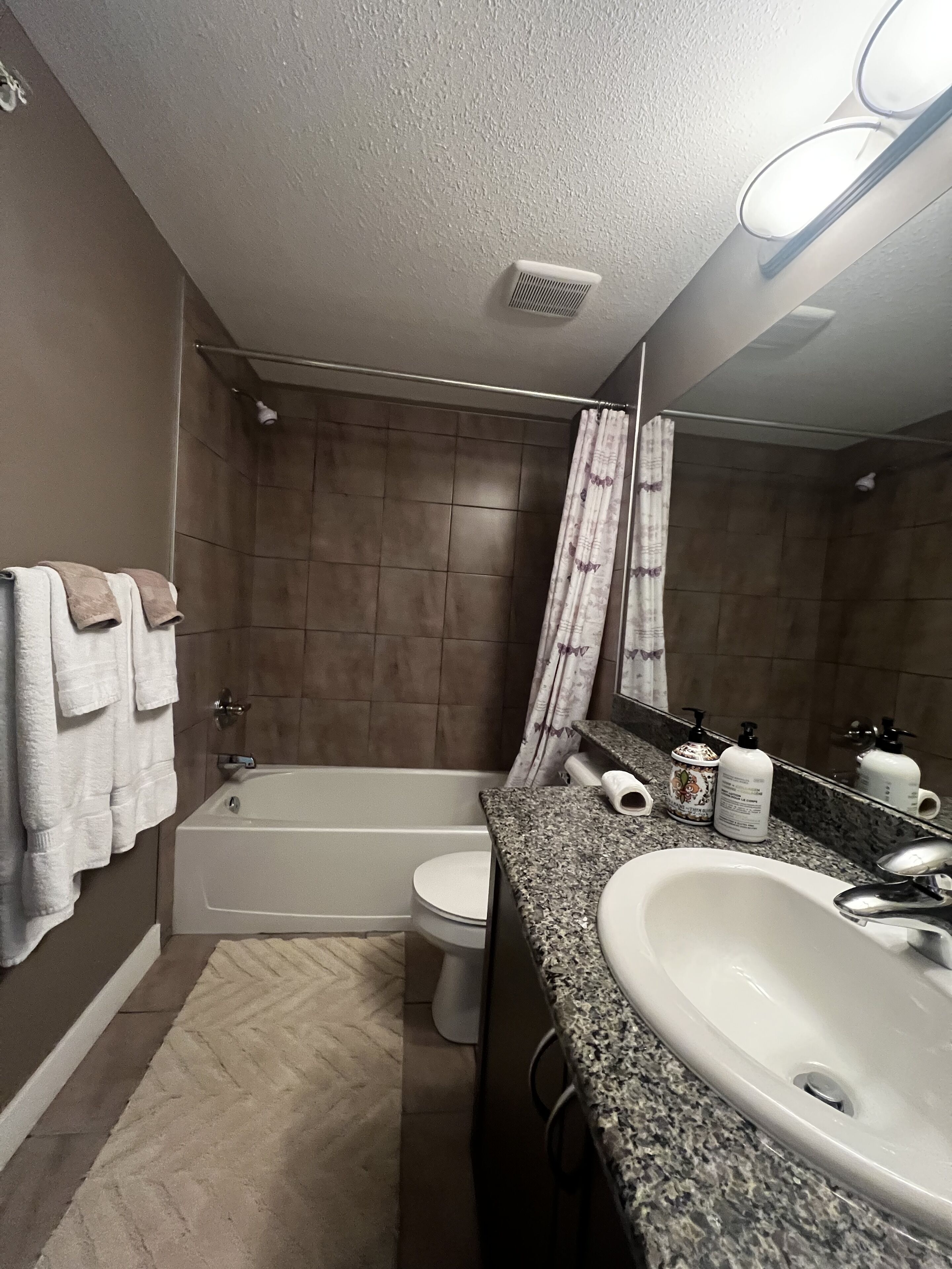 A bathroom with a bathtub, toilet, and sink. There are towels on the wall and a shower curtain.