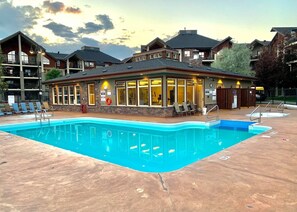 A pool area with a building that has large windows and a covered patio.