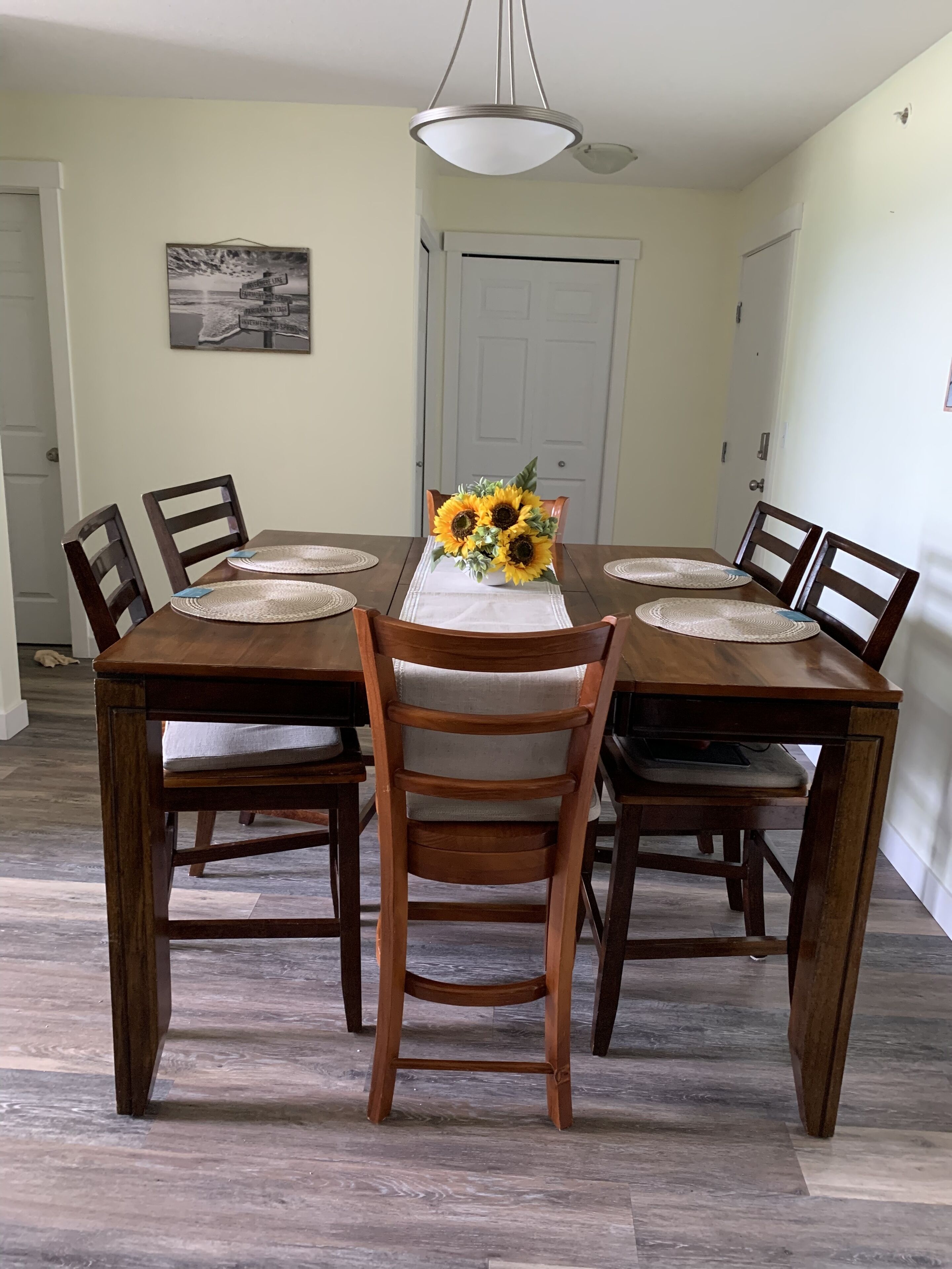 A dining table with four chairs, a vase of sunflowers, and a hanging light fixture.