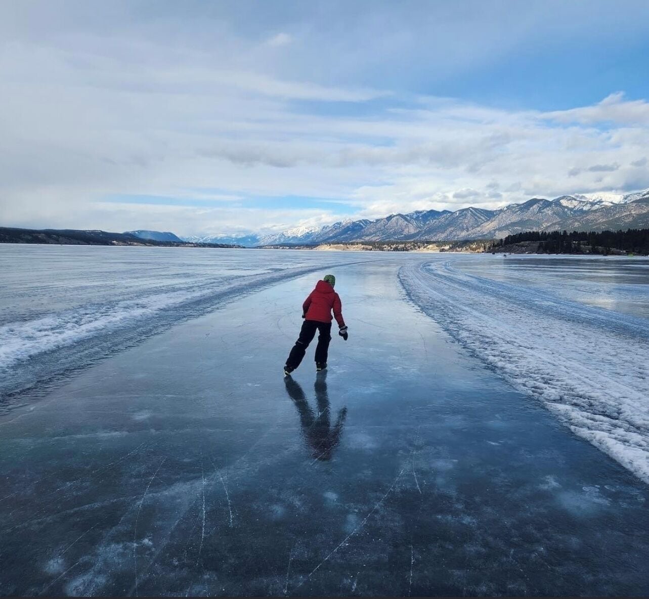 Una persona pattina su un lago ghiacciato, con montagne sullo sfondo.