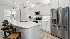 Una cocina moderna con armarios blancos, electrodomésticos de acero inoxidable y una isla central con taburetes de bar.