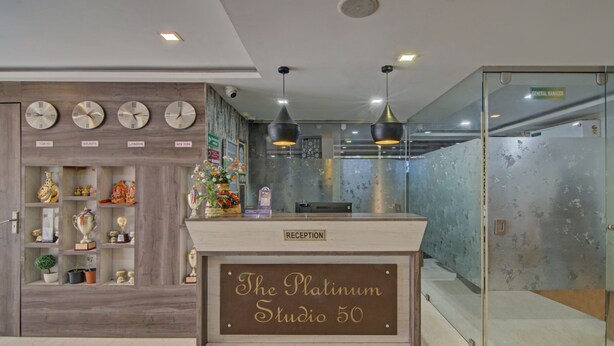 A reception desk labeled "The Platinum Studio 50" with clocks on the wall and a glass door to the right. - Treebo The Platinum Studio 50 (Barasat)