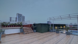 A rooftop terrace with wooden flooring, potted plants, a green hedge, and a metal pergola. - Treebo The Platinum Studio 50 (Barasat)