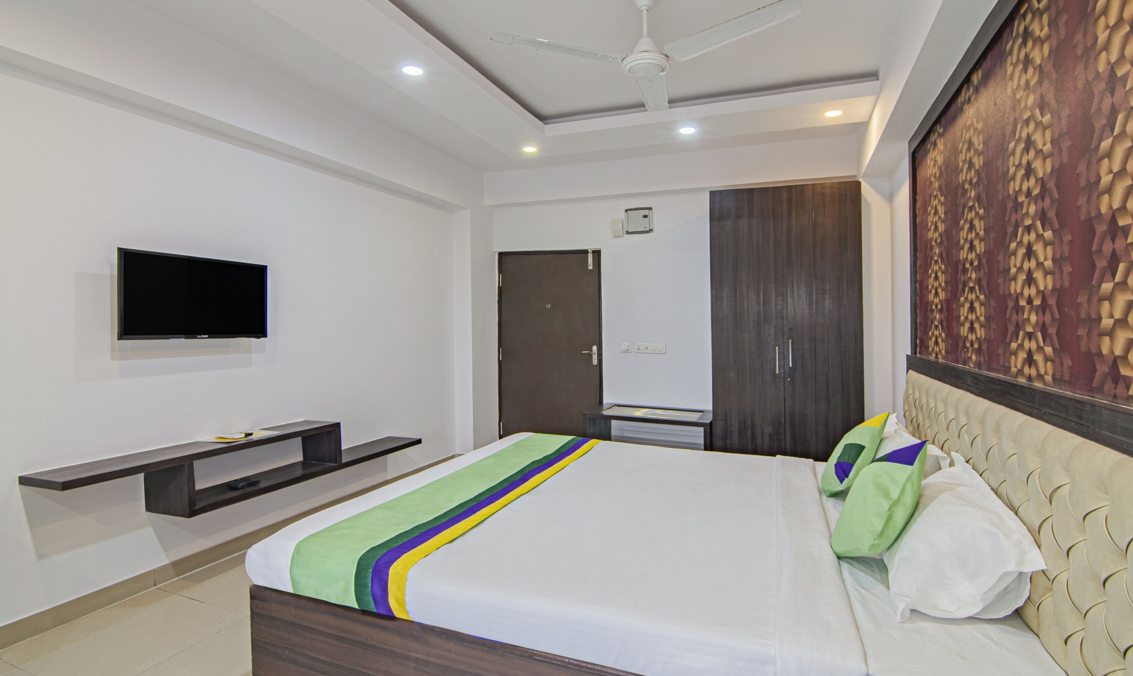 A modern hotel room with a bed, a flat-screen TV, a wardrobe, and a ceiling fan.
