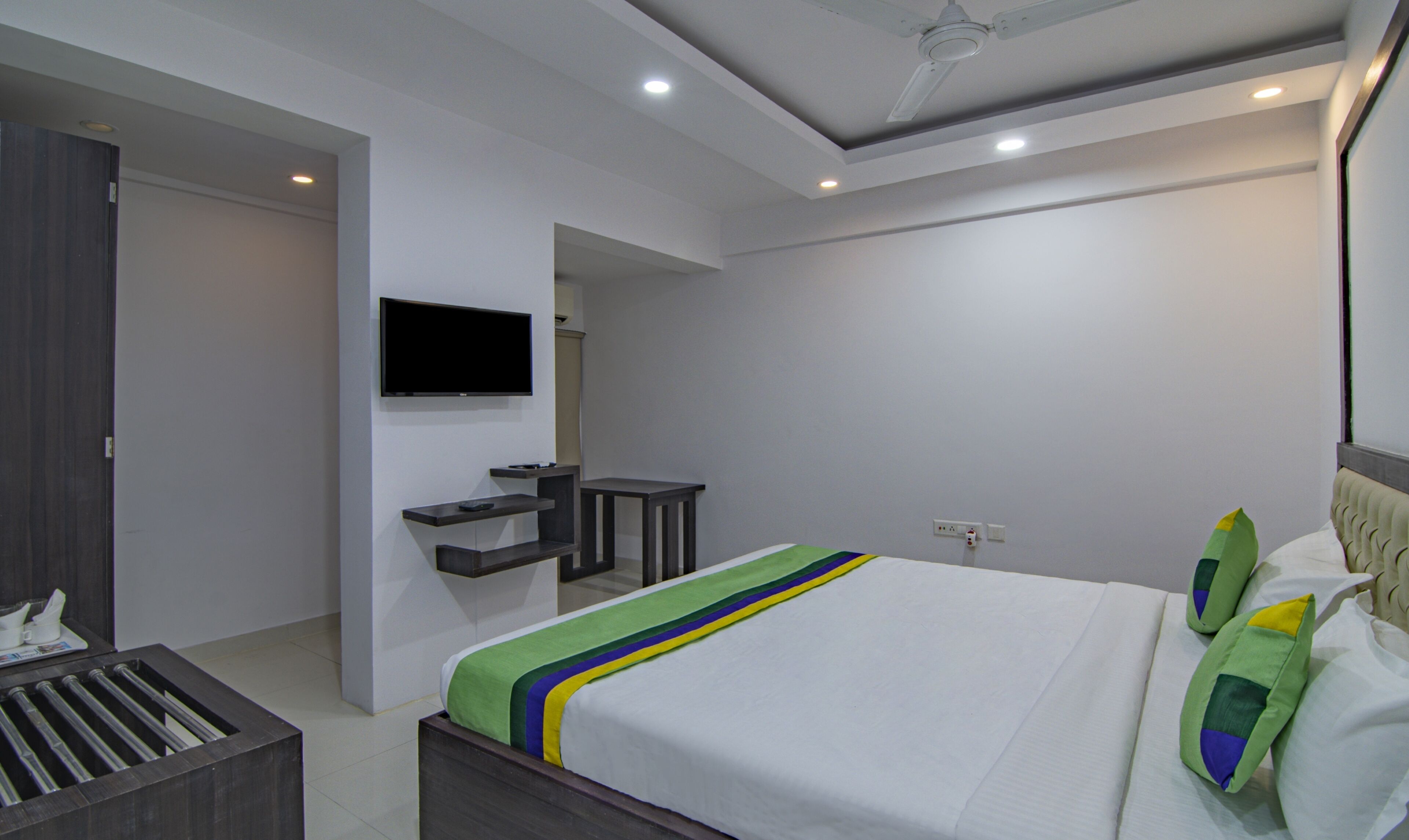 A modern bedroom with a bed, a TV mounted on the wall, and a small seating area.
