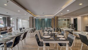 A modern dining area with glass tables and black leather chairs, featuring a view of the street through large windows. - Treebo The Platinum Studio 50 (Barasat)