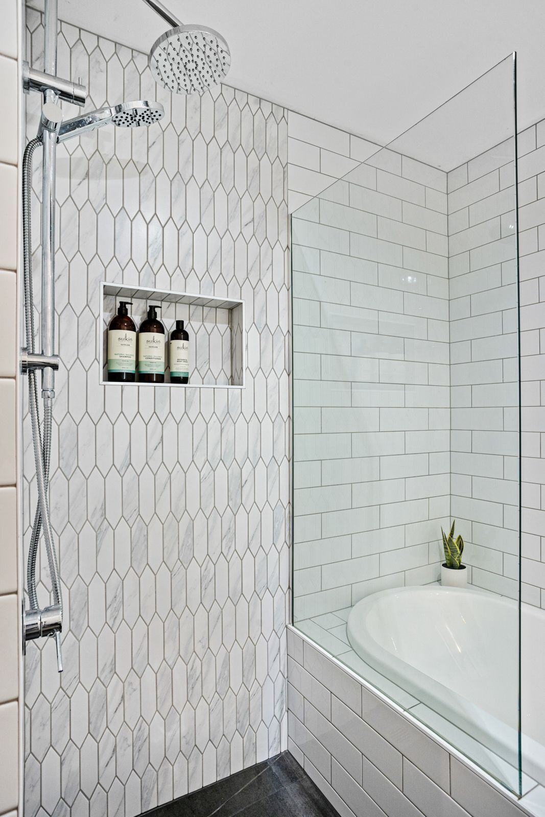 Un baño moderno con ducha, bañera con mampara de vidrio y repisas con artículos de tocador.
