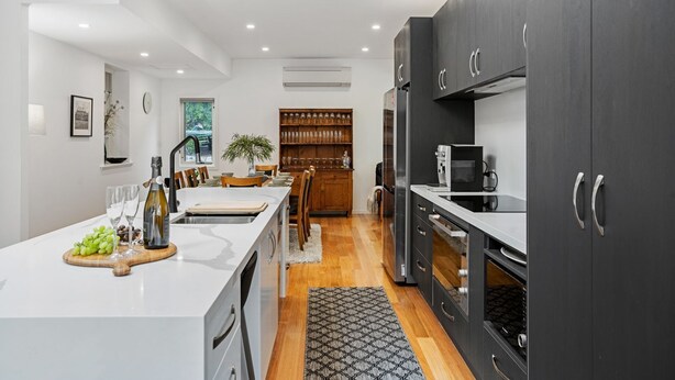 Una cocina moderna con una isla central, armarios oscuros y un comedor con sillas de madera y una vitrina de vidrio.