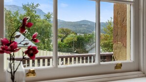 Una ventana con vistas a un paisaje montañoso, una cerca de madera y una casa al fondo.