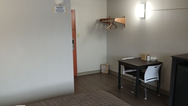 Ein Hotelzimmer mit einem Bett, einem Schreibtisch, einem Stuhl, einem Mülleimer und einer Wandleuchte.