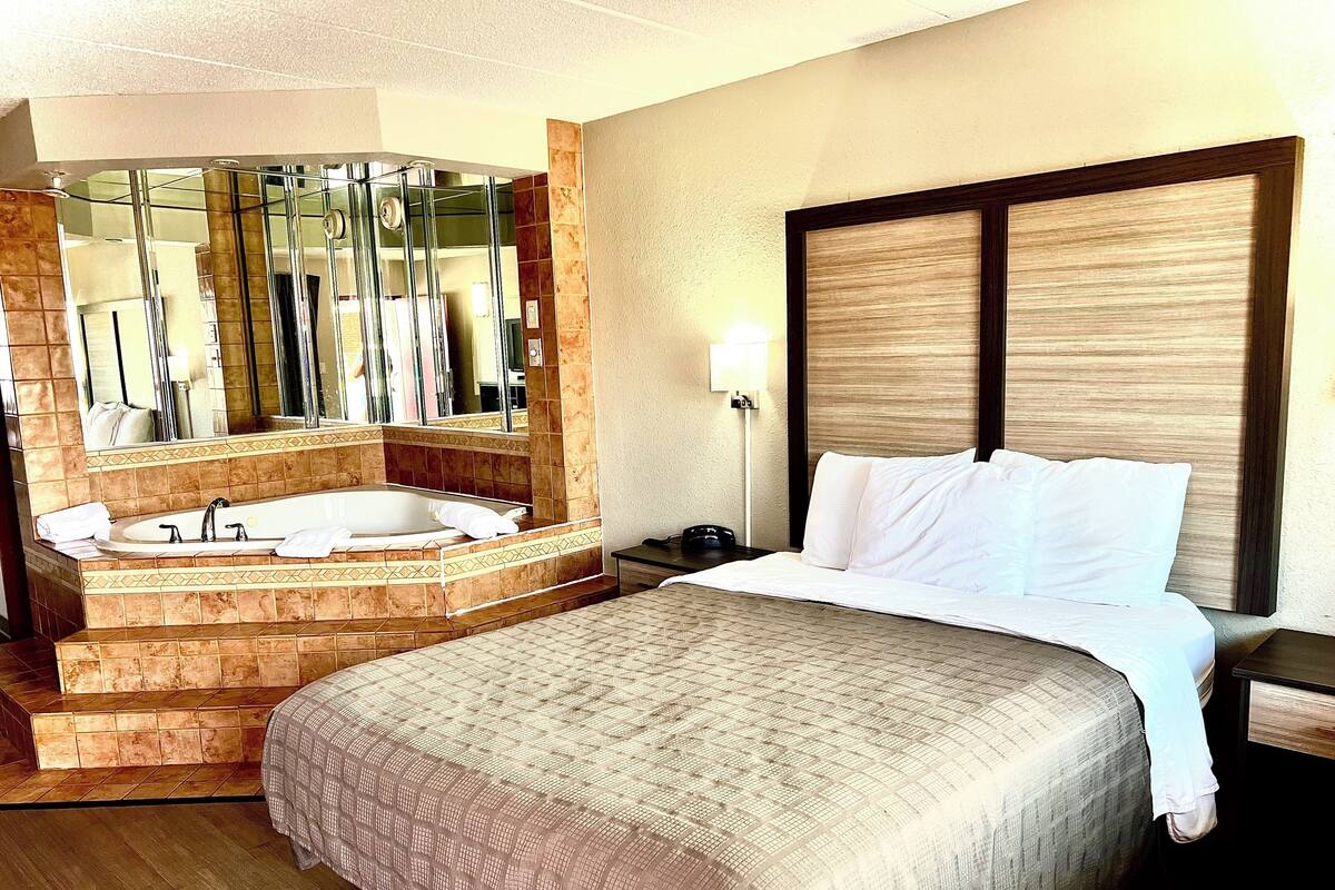 A hotel room with a large bed, a separate bathroom with a bathtub, and a large mirror.