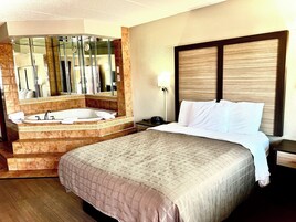Habitación de hotel con una cama grande, baño separado con bañera y un espejo amplio.