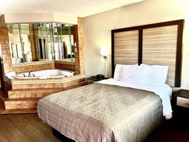 Habitación de hotel con una cama grande, baño independiente con bañera, un espejo amplio y una mesita de noche.