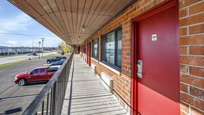 A building with a red door, a covered walkway, and a parking lot with cars. - Bridgeview Inn Chicago Area (Bridgeview)