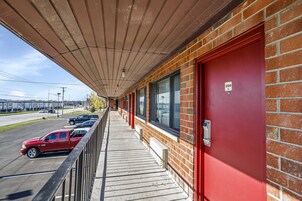 Un edificio con puerta roja, un corredor cubierto y un estacionamiento con coches.