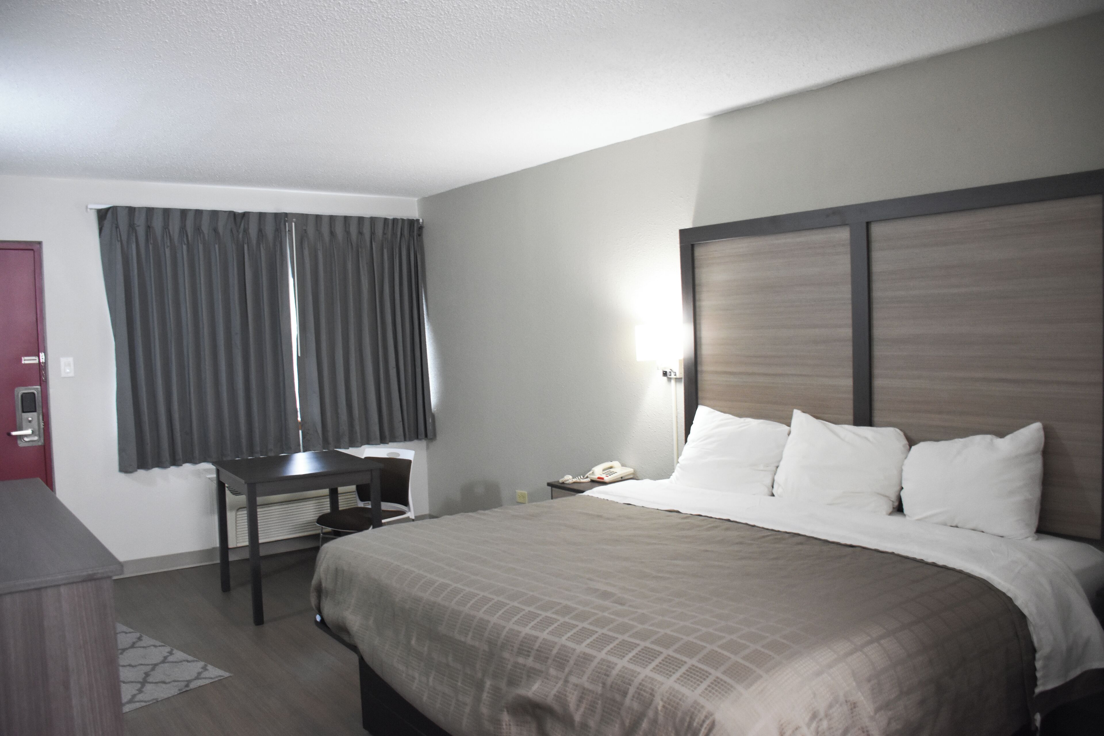 A hotel room with a large bed, a desk, a chair, a telephone, and a window with curtains.
