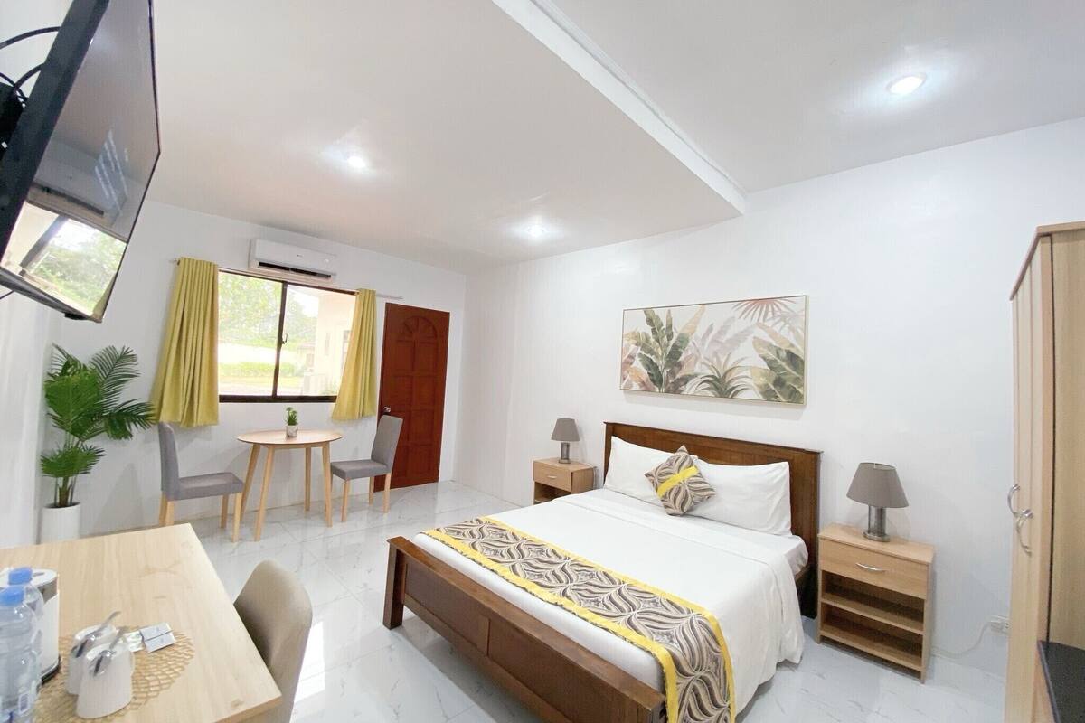 Habitación de hotel con cama, mesitas de noche, escritorio, silla, televisión y ventana con cortinas.