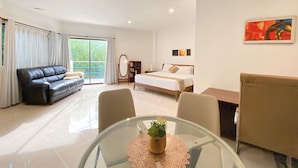 A modern hotel room with a bed, a sofa, a glass table with a plant, and a view of greenery through the window. - MVR Mariegold Resort Inc. (Lapu-Lapu)