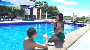A swimming pool with a tiled edge, a lounge area with chairs and tables, and a building with a door and windows in the background. - MVR Mariegold Resort Inc. (Lapu-Lapu)