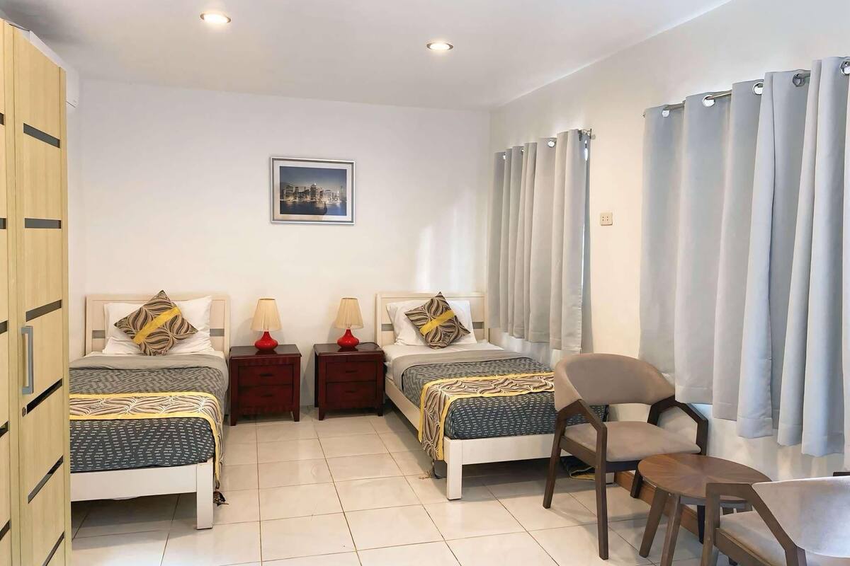 Habitación de hotel con dos camas, una silla, una mesa y un cuadro en la pared.