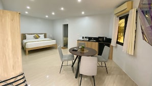 A modern hotel room with a bed, a dining table with chairs, a kitchenette, and a bathroom visible through an open door. - MVR Mariegold Resort Inc. (Lapu-Lapu)