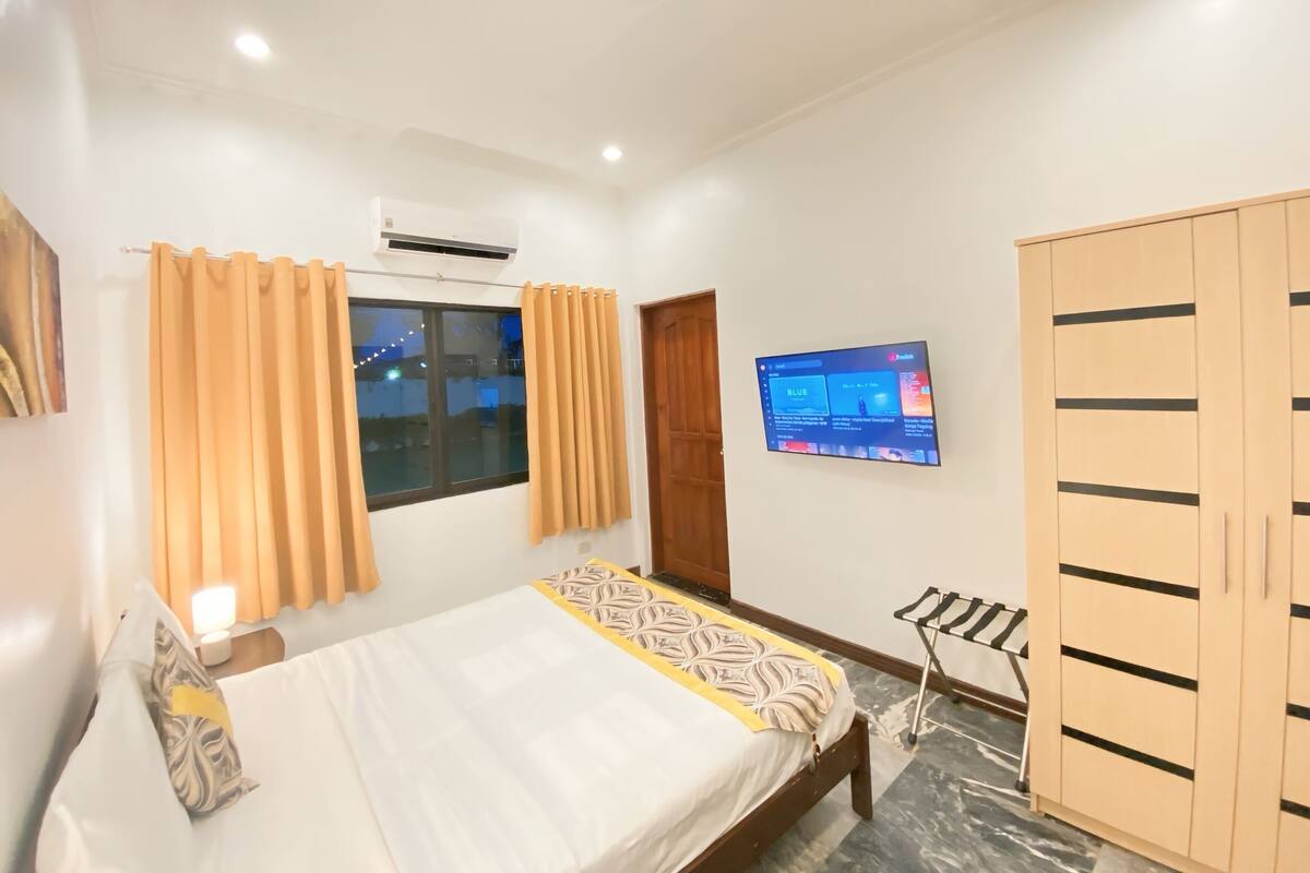 Un dormitorio con cama, cortinas, aire acondicionado, televisor y armario.