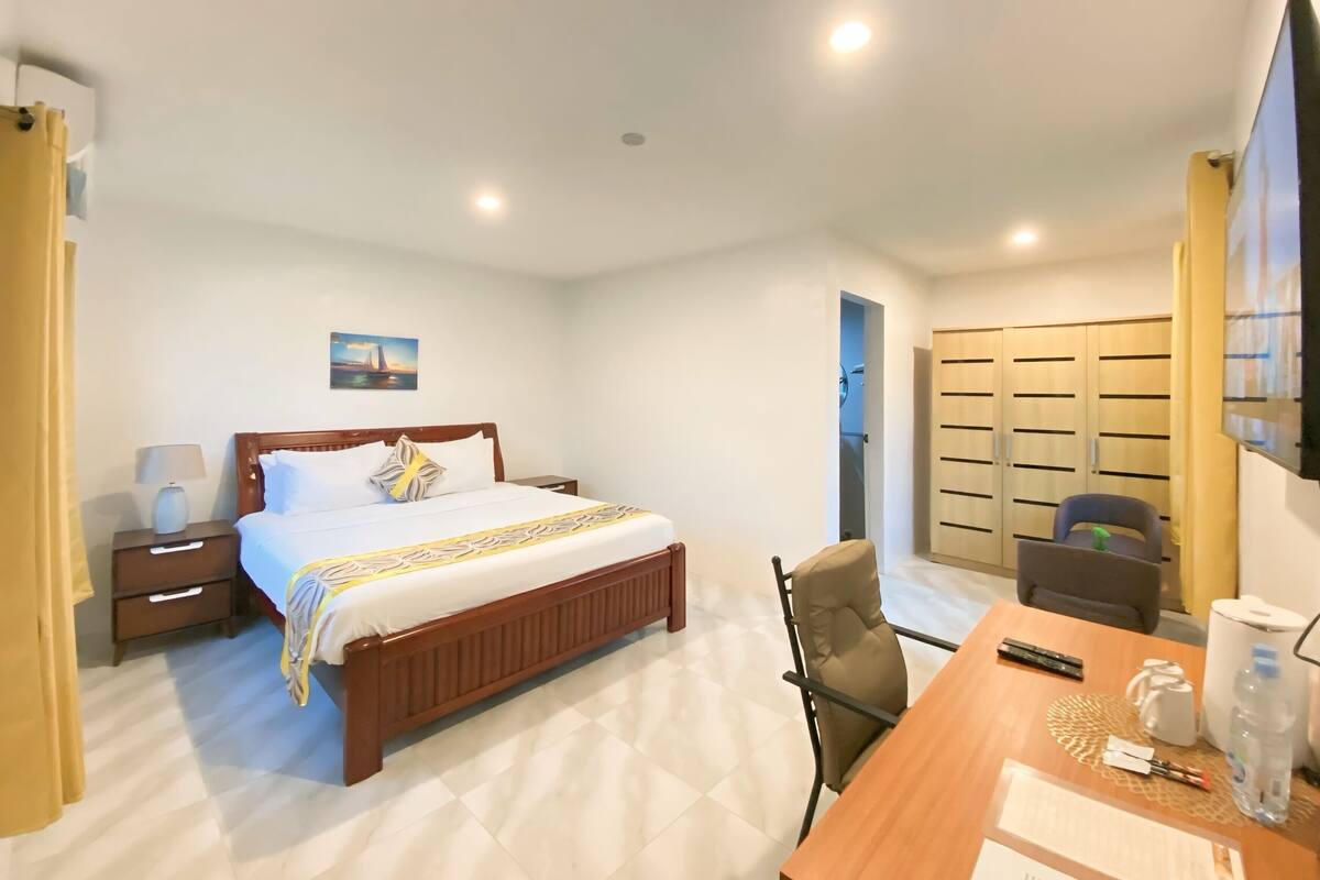 Habitación de hotel con cama, mesita de noche, lámpara, silla, escritorio y vistas al exterior.
