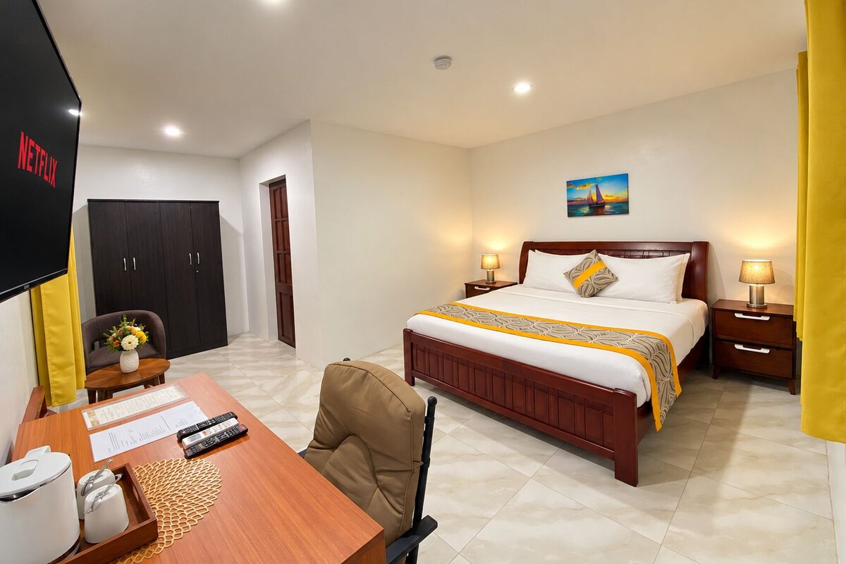 Una habitación de hotel con cama, mesitas de noche, escritorio con silla, televisor y armario.
