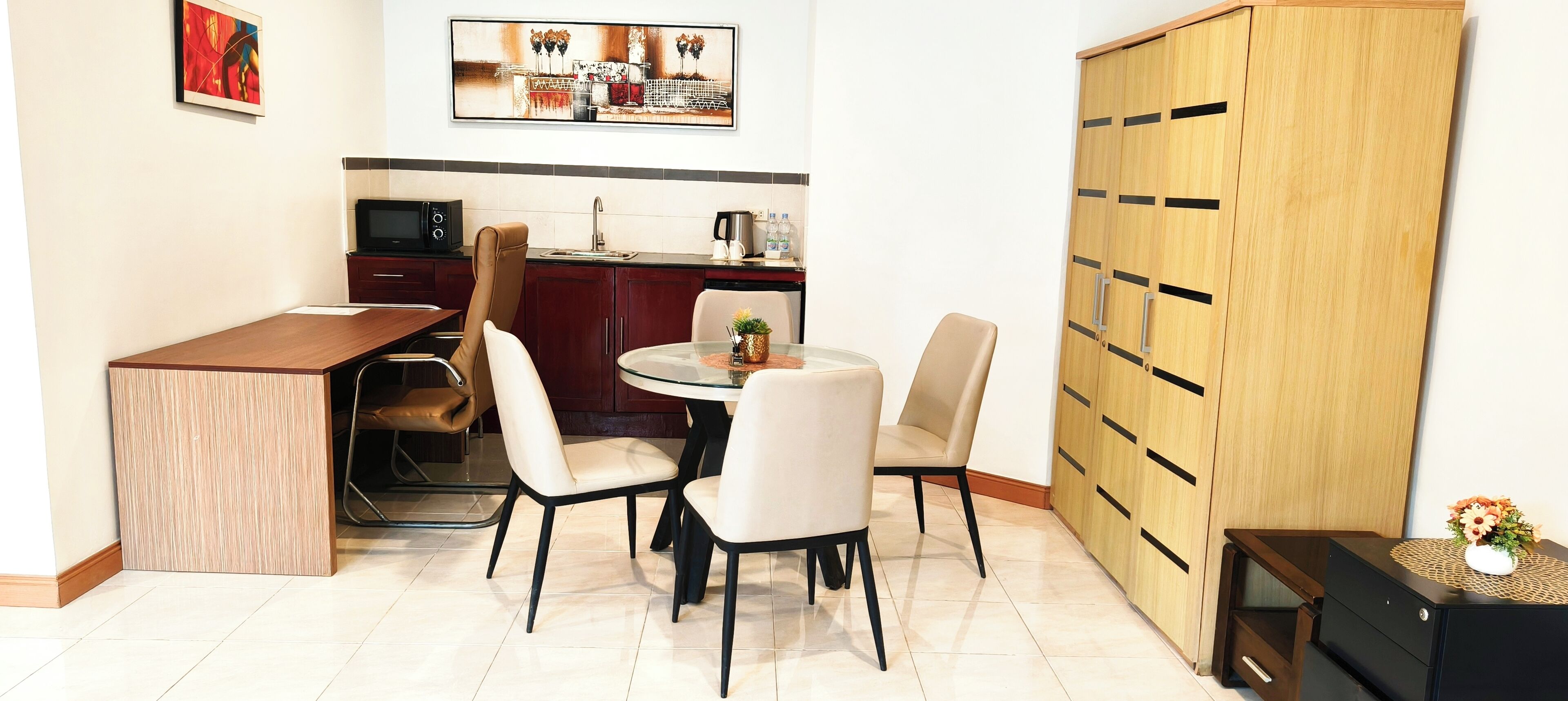 Cocina compacta con zona de comedor, que incluye una mesa redonda con sillas, un microondas y un mueble con cajones.