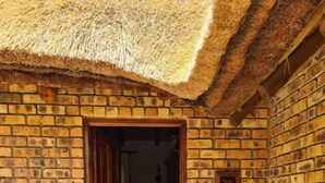 A brick building with a thatched roof entrance, a tiled floor, and a potted plant outside. - Khaya Africa Guesthouse and Spa (Midrand)