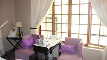 Una habitación con dos sillones morados, una mesita con artículos de aseo y una ventana con cortinas.
