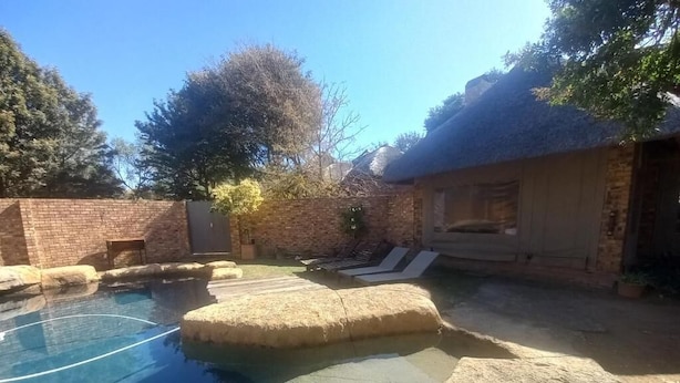 A swimming pool with a stone edge, lounge chairs, and a brick wall. - Khaya Africa Guesthouse and Spa (Midrand)