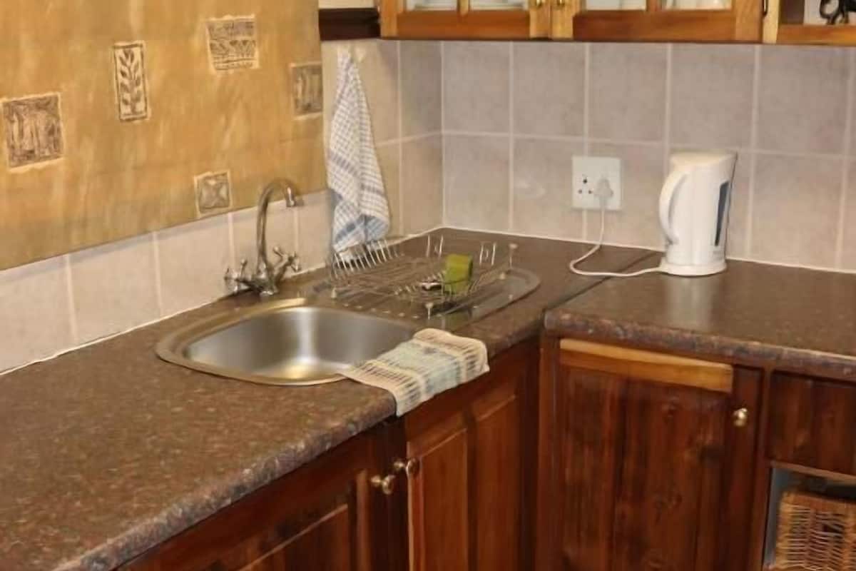 A kitchen with wooden cabinets, a stainless steel sink, and a kettle on the countertop.