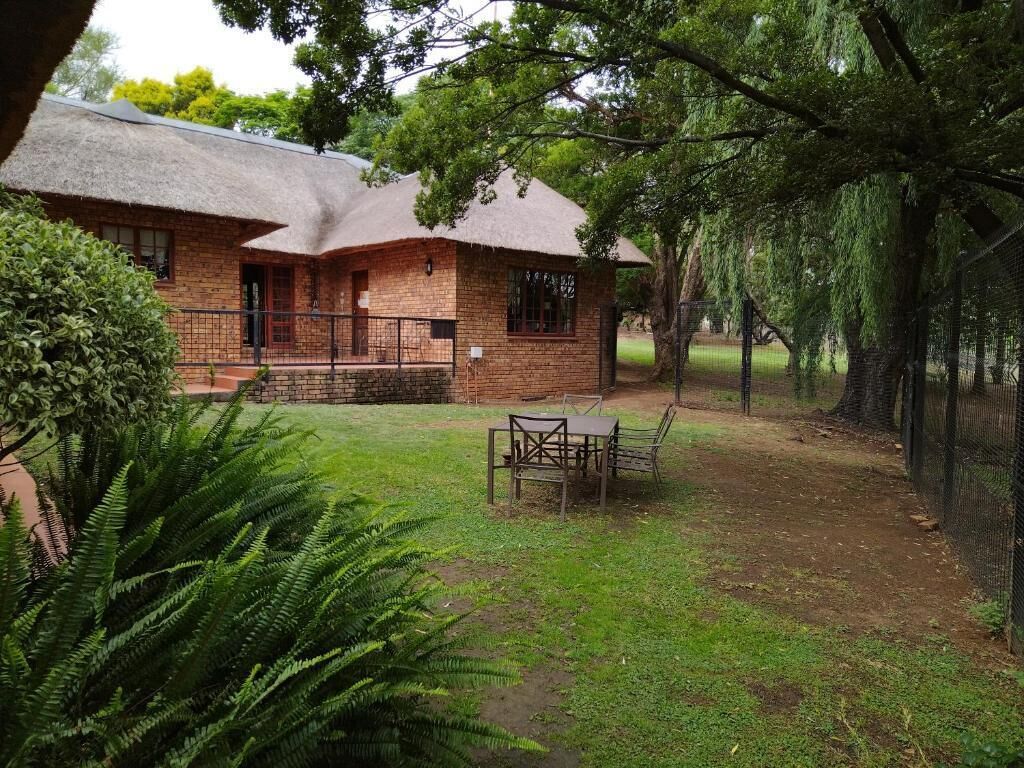 A brick building with a thatched roof, a fenced yard, and a table and chairs in the foreground.