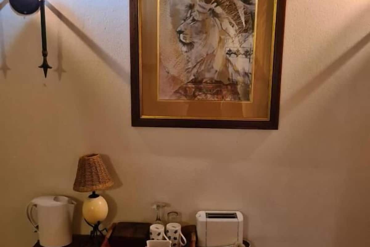 A framed artwork of a lion on the wall, a lamp, a pitcher, a toaster, and a chair in a room.