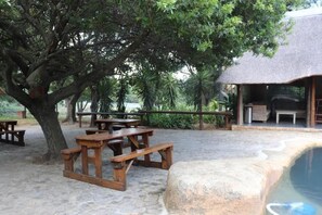Un espace extérieur aménagé avec des tables de pique-nique, une structure à toit de chaume et une piscine.