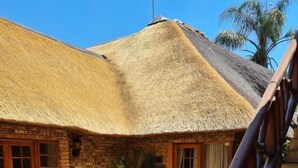 A thatched-roof building with a brick exterior, a stone patio, and a wooden staircase. - Khaya Africa Guesthouse and Spa (Midrand)