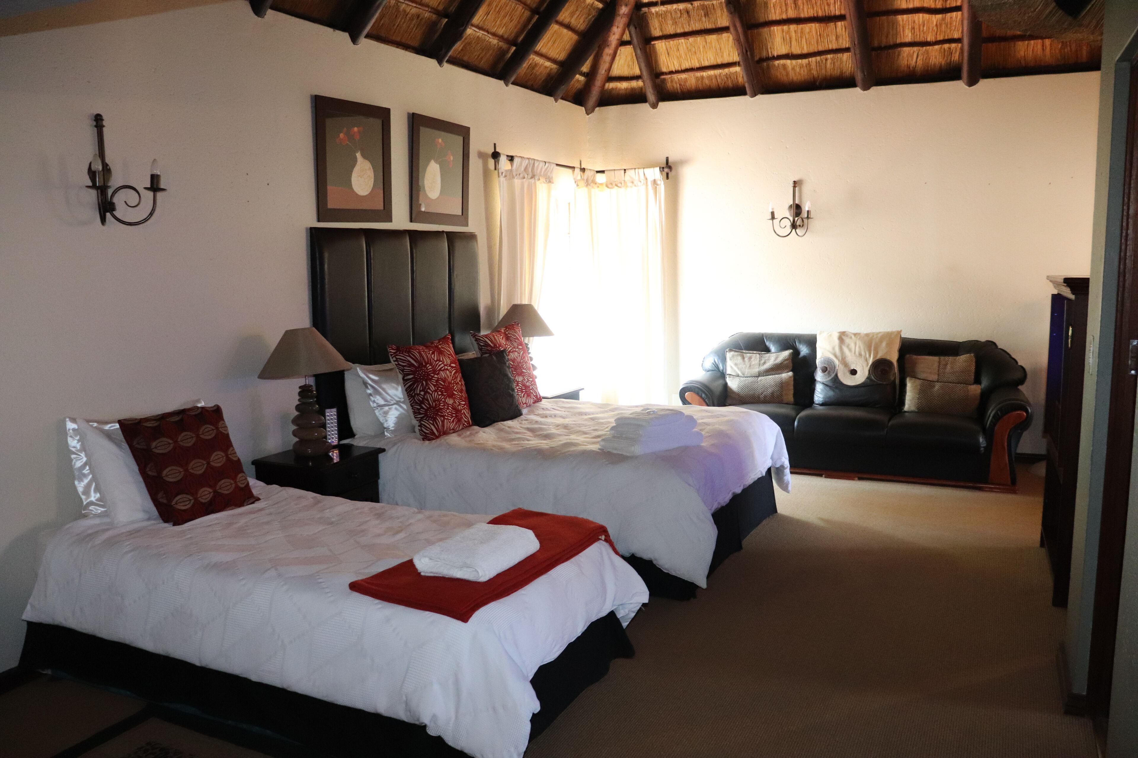 Habitación de hotel con dos camas, un sofá, una lámpara y un cuadro en la pared.