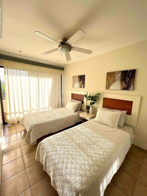 A hotel room with two beds, a ceiling fan, and artwork on the walls.