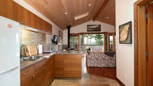 Eine moderne Küche mit Holzschränken, einem eingebauten Backofen und einer Arbeitswand aus Stein. Ein Essbereich mit einem Tisch und Stühlen mit Muster, und ein Blick ins Freie durch große Fenster.