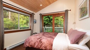 Ein Schlafzimmer mit einem großen Bett, Holzböden und Blick ins Grüne durch die Fenster.