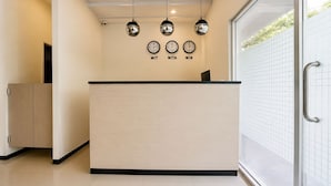 A reception desk with a light wood finish, three wall clocks above it, and a glass door to the right.