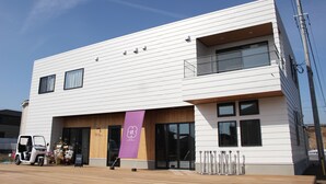 A modern two-story building with a flat roof, large windows, and a wooden deck in front. - Matoi Hostel & Bar (Takasaki)