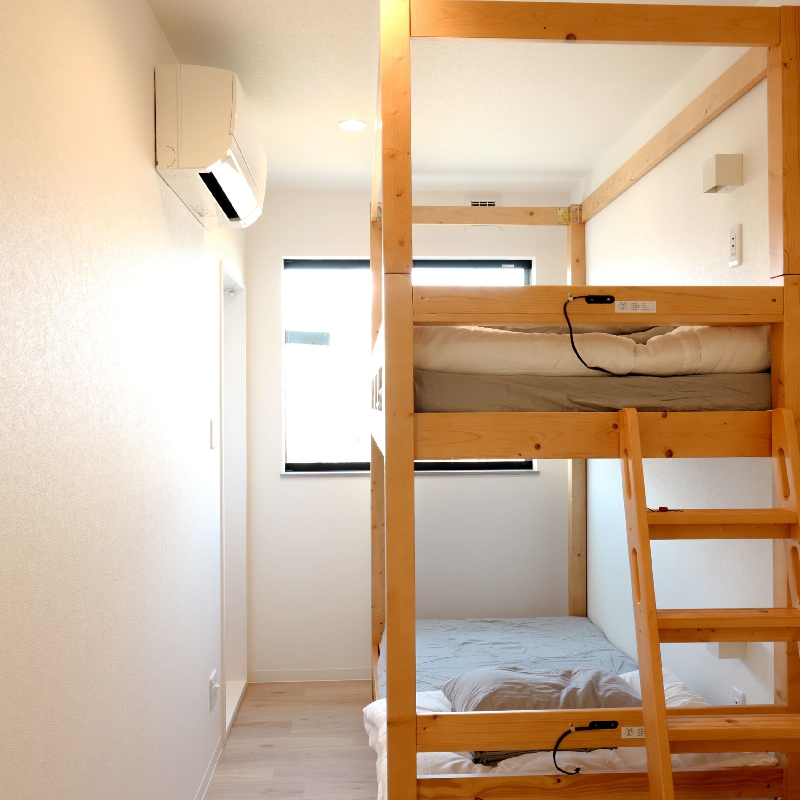 Habitación con literas, ventana, aire acondicionado instalado en la pared y suelo de madera.