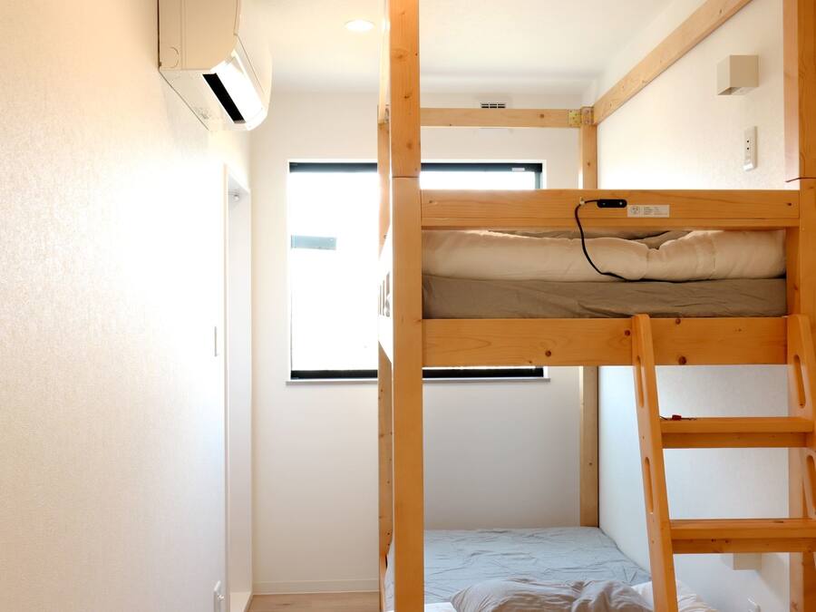 Habitación con literas, ventana, aire acondicionado instalado en la pared y suelo de madera.