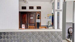A building entrance with a wooden door, a reception desk, and a tiled wall. - OYO 90405 Penginapan Sasti KuninganNearTaman Cirendang (Cilimus)